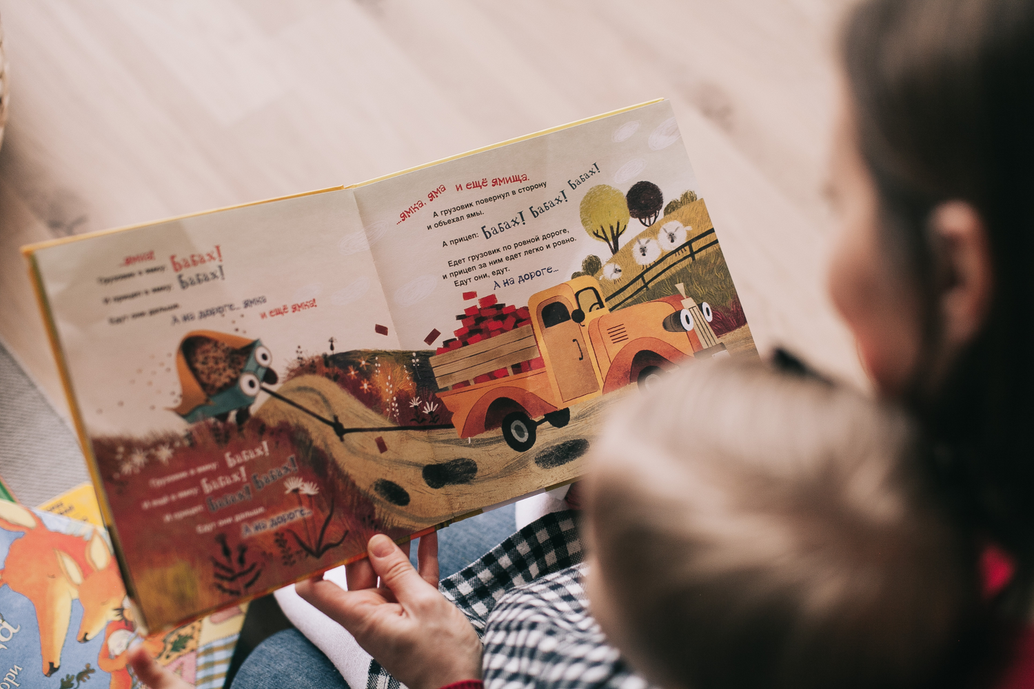 Close-up of a child and an adult reading a colorful children's book together, featuring a whimsical illustration of animals in a truck.