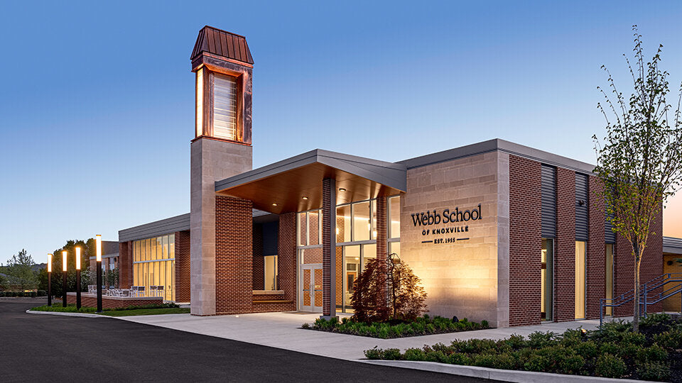 Modern exterior of Webb School of Knoxville at dusk, featuring contemporary brick and glass architecture with illuminated tower and landscaping.